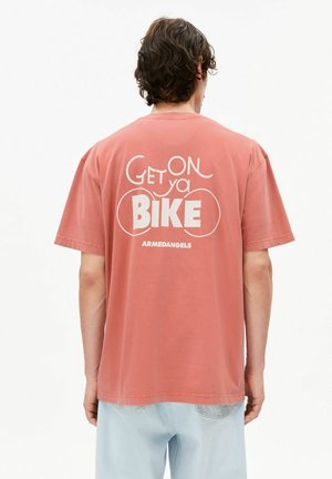 T-shirt en coton rose avec manches courtes, portant un texte blanc disant "Get ON ya BIKE" et le nom de la marque "ARMEDANGELS" au dos.