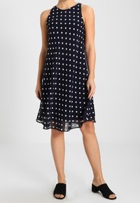 Mörkblå ärmlös klänning med vita prickar, svängande nederkant och lätt tyg. Matchas med svarta slip-on skor.