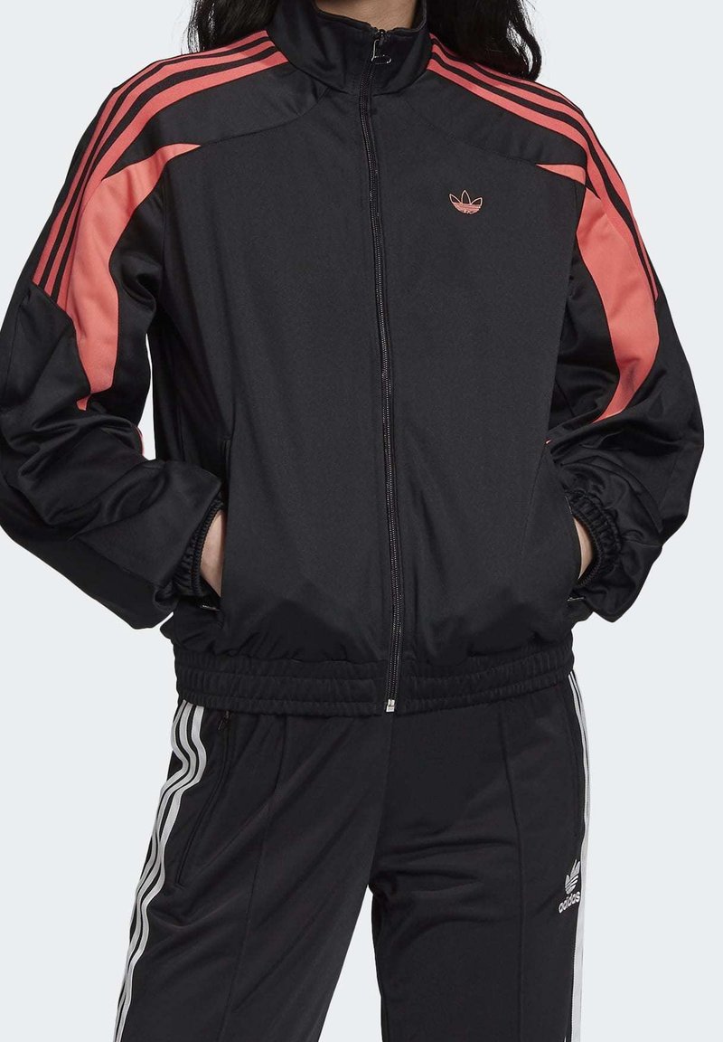 Svart träningsjacka med rosa ränder, dragkedja framtill, hög krage, elastiska mudd och fåll, med en Adidas-logotyp på bröstet.