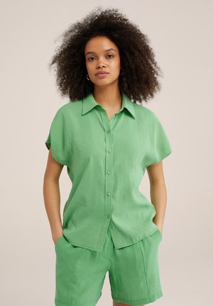 Grön kortärmad skjorta med knappar i lätt material, tillsammans med matchande gröna shorts. Slät textur, avslappnad passform och diskret krage.