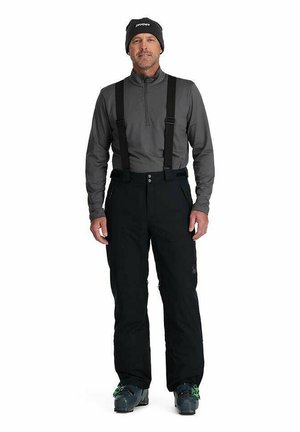 Black waterproof snow pants with adjustable suspenders, worn over a gray long-sleeve top, paired with gray ski boots.