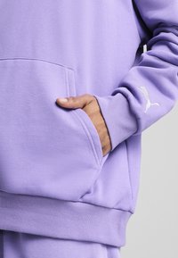 Lavender sweatshirt med en kengurulomme og ribbede manchetter. Har et lille hvidt Puma-logo på venstre håndled. Blødt, struktureret stof.