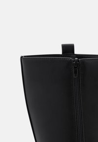 Svart läderankelstövel med slät yta, sidoförslutning med dragkedja och en ögla högst upp för enkel påklädning.