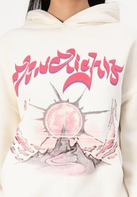 Cream hooded sweatshirt featuring a colorful graphic design with a sun and mountains. The pattern combines pink and gray tones with intricate details.