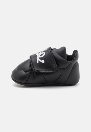 Chaussure en simili cuir noir avec un bout rond, une sangle Velcro et des détails de couture subtils. Doublure intérieure douce pour le confort.