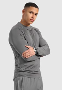 Graues, langärmliges Sportshirt aus einem glatten, leichten Stoff, schlanker Schnitt und subtilen Nähten. Mit Rundhalsausschnitt und Etikett am Ärmel.