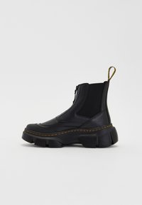 Černé kotníkové boty s robustní podrážkou, vyrobené z kůže a elastických materiálů. Mají boční zip a žluté švy jako akcenty.