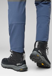 Schwarze Wanderschuhe mit strukturiertem Obermaterial, grauen Sohlen und reflektierenden Akzenten. Vibram-Logo auf der Laufsohle für besseren Halt.