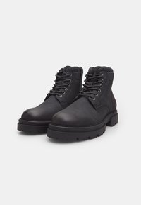 Botines de cuero negro con cuello de tela texturizada, ojales metálicos y suelas de goma gruesas para mayor tracción. Presentan punta redondeada y diseño de cordones.