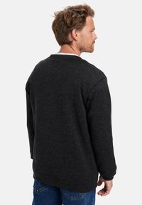 Sudadera gris oscuro con cuello redondo, tejido texturizado, mangas largas y un corte holgado, combinada con jeans azules. Diseño sencillo.