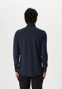 Camisa de manga larga azul marino, tela texturizada, puños con botones, dobladillo curvo y cuello clásico, con sutiles patrones geométricos.