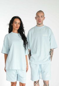 Svetle modré oversized trička s krátkým rukávem, doplněná o odpovídající šortky. Obsahuje jemný bílý text s logem a hladkou texturu látky.