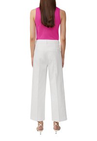 Pantalon large blanc en tissu léger, associé à un top sans manches fuchsia, mettant en avant une texture lisse et des lignes épurées.