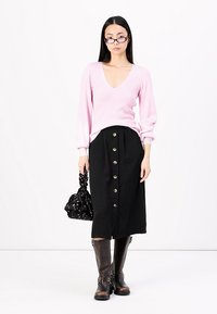 Blusa de manga longa canelada rosa clara com decote em V, combinada com uma saia preta de botão, botas de pele castanhas até ao joelho e uma mala preta com flores.