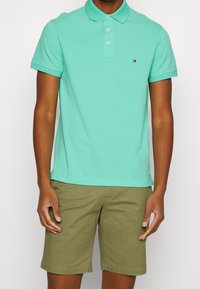 Polo vert menthe avec un col classique, patte de boutonnage à deux boutons et petit logo sur la poitrine. Assorti avec un short kaki. Tissu en coton.