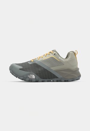 Grijze en beige sport schoenen met een gestructureerde bovenkant, verstevigde neus, gele accenten en een gestructureerde rubberen zool voor grip.