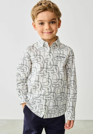 Biała koszula z długim rękawem z czarnymi geometrycznymi wzorami w kształcie litery "B" oraz napisem "BAKER". Posiada kołnierz na guziki i lekko zaokrąglony dół.