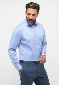 Helleblaue Langarm-Hemd mit Knöpfen und spitzem Kragen, glatter Textur und weißen Knöpfen. Kombiniert mit dunkelblauen Hosen.