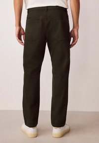 Tumed rohelised sirged püksid, kahe tagataskuga ja siledast kangast, millele on lisatud valged tossud heledal taustal.