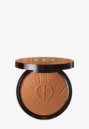 Bronzer in un compact rotondo con un coperchio marrone lucido e una texture a raggi di sole. Presenta un logo impresso al centro con dettagli dorati.