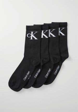 Black cotton socks featuring a ribbed cuff, cK logo in white on the front, and branding on the sole; includes four pairs in total.