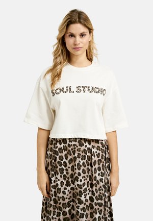 Gekürztes cremefarbenes T-Shirt mit "SOUL STUDIO" im Leopardenmuster, kombiniert mit einem braunen Leopardenmuster-Rock, der eine lockere Silhouette und eine weiche Textur aufweist.