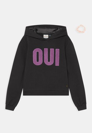 Schwarzer Kapuzenpullover mit auffälligem lila "OUI"-Schriftzug. Weicher Stoff, cropped Design und gerippte Bündchen. Einschließlich eines hellrosa Haargummis.