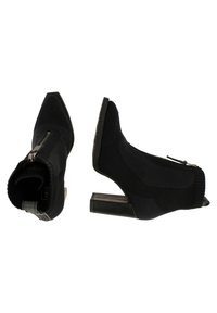 Bottines noires style chaussette avec talons blocs, bouts pointus et zips latéraux, présentées en vues de dessus et de côté sur fond blanc.