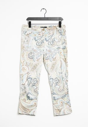 Světlé kalhoty s detailním paisley vzorem v modrých, béžových a hnědých tónech zavěšené na černém klipu na ramínku na bílém pozadí.