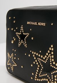 Sort lædertaske med guldstjerneprydelser og nitter, med et guld "Michael Kors" logo på forsiden for ekstra detalje.
