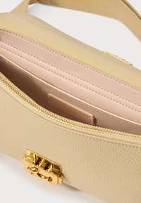Μπεζ δερμάτινη τσάντα με υφή, χρυσά μεταλλικά στοιχεία και κλείσιμο με φερμουάρ. Το εσωτερικό διαθέτει λεία ροζ επένδυση και ετικέτα επωνυμίας.