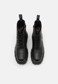 Bottes de cheville en cuir noir avec un bout arrondi, un laçage à l'avant et une semelle épaisse. Comprend des fermetures éclair latérales et des languettes en tissu.