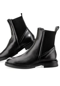 Paire de bottines Chelsea en cuir noir avec panneaux latéraux élastiques et languettes de tirage sur fond blanc.
