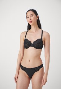 Svart spets-bh med scallopade kanter, med underwire-stöd och justerbara straps, parat med svart bikinitrosa med spetsdetaljer.