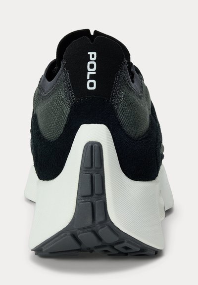 Zapatilla negra y gris con suela blanca vista desde el talón, mostrando la marca "POLO" en el cuello trasero.