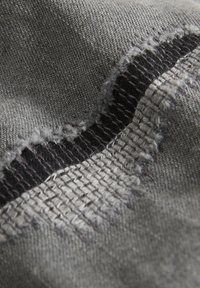 Textilpatch mit einer strukturierten, grauen Stofffläche mit Wellenmuster, kontrastierenden schwarzen Nähten und ausgefransten Kanten für ein rohes Finish.