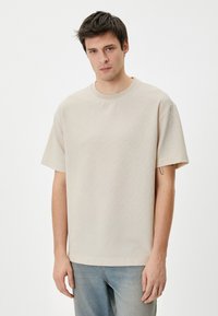 Beige bomulds t-shirt med rund hals og korte ærmer i struktureret stof. Båret med lys blue denim jeans.