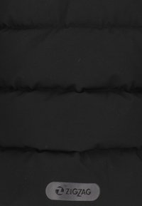 Schwarze Pufferjacke aus Material mit gesteppten Abschnitten; zeichnet sich durch eine strukturierte Oberfläche und ein sichtbares "ZIGZAG"-Logo auf einem abgerundeten grauen Badge aus.