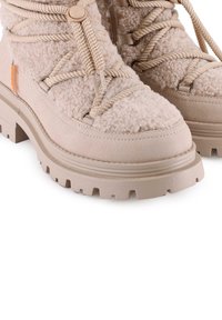 Botas de senderismo beige con parte superior de tejido de felpa texturizada, suela de goma resistente con un profundo perfil y detalle de cordones en contraste.