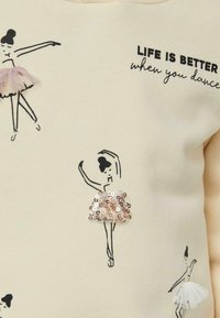 Bocetos de bailarinas de ballet con faldas de tela y lentejuelas sobre tela crema, acompañados del texto "La vida es mejor cuando bailas."