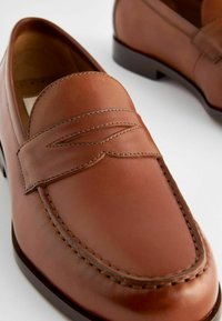 Braune Leder-Laufflächen mit einer geschwungenen, gestickten Akzentuierung. Glatte Textur, niedriger Absatz und ein abgerundetes Design der Zehenpartie. Klassischer Schlupfstil.