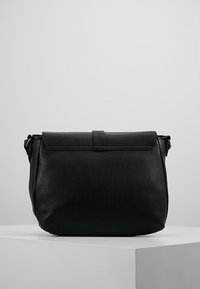 Borsa a spalla in pelle nera con una consistenza morbida, forma rettangolare, chiusura a pattina e una singola tracolla regolabile. Dettagli in metallo dorato.