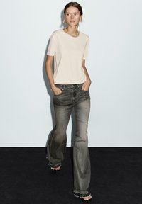 T-shirt rosa chiaro a maniche corte abbinato a jeans a campana grigi sbiaditi. I jeans presentano orli sfrangiati e due tasche frontali. Design semplice.