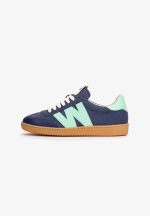 Zapatilla de caña baja azul marino con "W" en verde claro y acentos en el talón, cordones blancos y suela de goma color caramelo, vista desde el exterior.