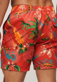 Pantaloni da bagno rossi realizzati in tessuto leggero, caratterizzati da una stampa tropicale con palme, fiori e tavole da surf. Vita elasticizzata, tasche laterali.