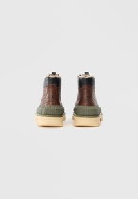 Zapatillas altas de cuero marrón y negro con una media suela verde texturizada y una suela externa color beige claro. Cuentan con un forro suave y una lengüeta.