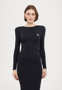 Mustarikk pikikätel dress, mis on sobiva siluetiga. Pehme ja veniv kangas; rinnal väike broderingustatud logo. Minimalistlik disain.