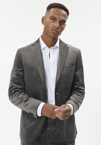 Pelēka samta žakete ar izgrieztiem laciem, vienu pogu un kabatas lakatiņu. Uzvilkta virs baltas pogām aiztaisāmas krekls.