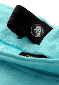 Türkiser Stoff mit einer weichen Textur, versehen mit einem schwarzen elastischen Band und einem transparenten Knopf mit einem floralen Design in der Nähe eines inneren Etikettes.