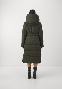 Tmavě zelený prošívaný kabát s kapucí, páskem v pase, délkou do poloviny lýtek a prošívanou texturou. Navržen s velkým polstrováním a bez viditelné kovové výbavy.